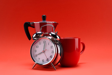 close up view of coffee maker, alarm clock and cup of coffee isolated on red