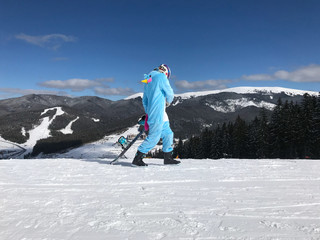 Girl in blue, pink unicorn pajama kigurumi outdoor with snowboard on the ski report in snow mountains.
