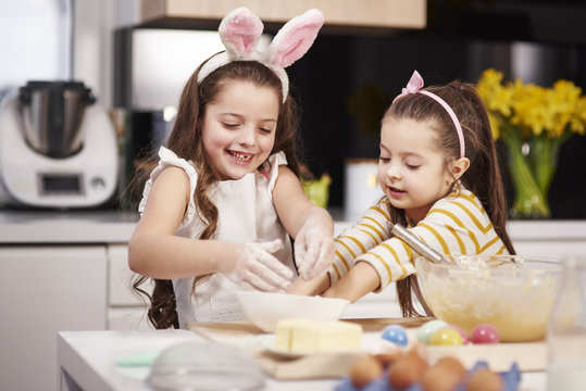 Two sisters having fun baking Easter cookies in kitchen together