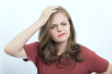 Portrait of blonde girl or young woman wearing red t-shirt with perplexed, puzzled, dumb, ignorant expression on her face scratching head with hand. When you don't know the answer
