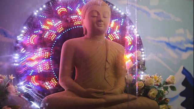 Buddha statue surrounded by flashing colorful festive lights on an abstract background in a Buddhist temple.