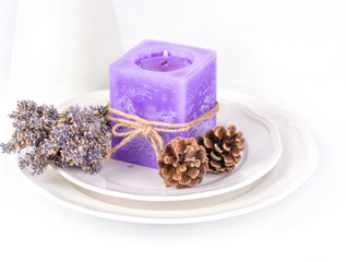 Still life with lavender candle, fir cones and dry lavender on a white plate on white background.