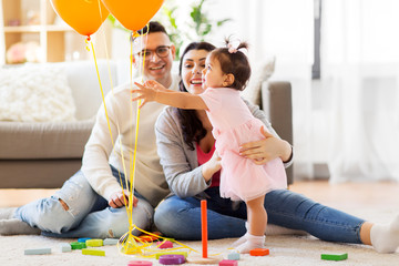 family, holidays and people concept - happy mother, father and little daughter reaching to balloons at home birthday party