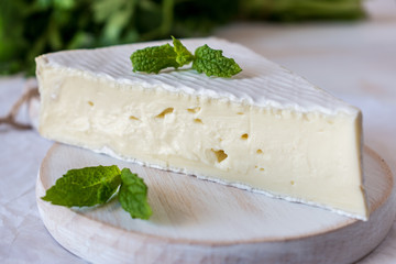 Fresh Brie cheese on white wooden board.