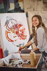 Artistic girl sitting in studio and paint on easel.