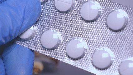 A pharmacist holds pills, blue rubber gloves, a white background.