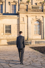 Back view of the elegant young man who is walking at the palace