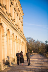 Back view of the young couple and young man near them who are walking together by the palace