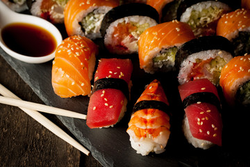 Sashimi and sushi rolls on a stone slatter. Sushi set with salmon, prawns, soy souce, wasabi and ginger. Traditional Japanese cuisine.