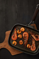 top view of grilled shrimps on wooden cutting board on black tabletop