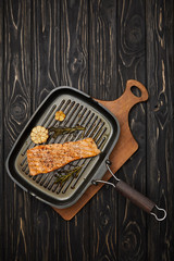 top view of arranged grilled salmon steak with rosemary on cutting board on black wooden tabletop