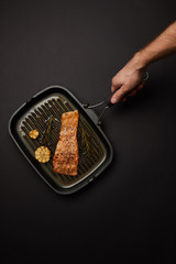 cropped shot of man holding grill with salmon steak on black tabletop
