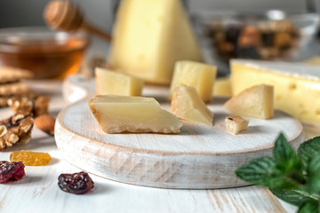 Fresh Greek cheese graviera and a slice on white wooden board with nuts, honey and herbs.