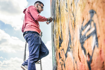 Tattooed graffiti writer painting with color spray on the wall