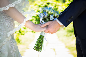 Hands of loving couple holding a wedding bouquet of white roses flowers.
