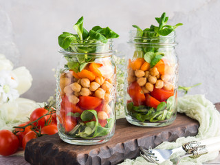 Fresh salad lunch with chickpeas, tomatoes, carrots and valerian served in mason jars