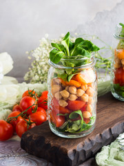 Fresh salad lunch with chickpeas, tomatoes, carrots and valerian served in mason jars