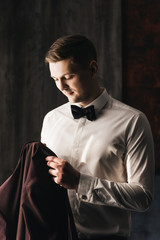 Morning of the groom. Good morning preparation. Young and handsome groom in a wedding shirt holds a jacket in a beautiful interior