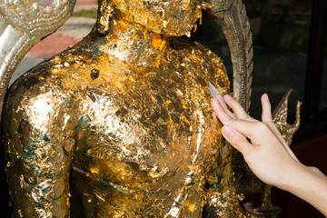 Closeup Girl hands Put gold leaf onto The Buddha statue, Gilded Buddha statue, Buddhists make merit, Selective focus