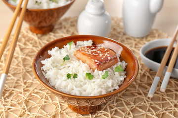 Fish fillet served with rice in brown bowl on knitted coaster
