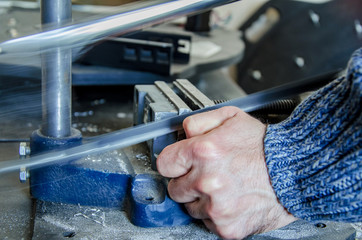 Man's hand is sawing a metal in a vice with a hacksaw