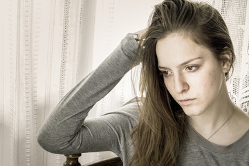 Young girl sad at home with a hand on her head looking away.