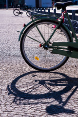 The rear wheel of a bicycle casts a shadow on the cobbled path