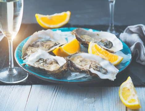 Fresh Oysters closeup on blue plate, served table with oysters, lemon and ice. Healthy sea food. Oyster dinner with champagne in restaurant. Gourmet food