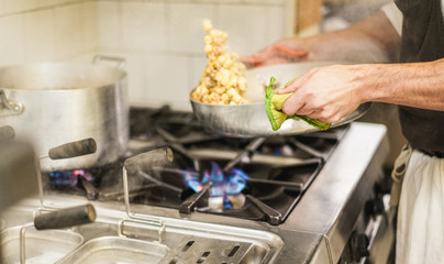 Male chef mixing with sauce fresh homemade pasta in restaurant kitchen
