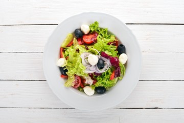 Salad with mozzarella and fresh vegetables. On a white wooden background. Top view. Copy space for your text.