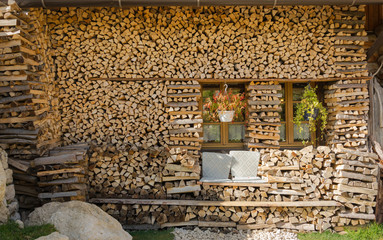 Summer cottage in village in Alps with big pile wood, grey stone, two windows and handmade seats for relax