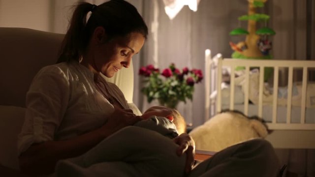 Young beautiful mother, breastfeeding her newborn baby boy at night, dim light. Mom breastfeeding infant