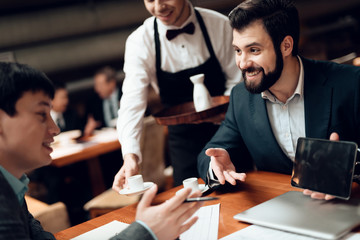 Meeting with chinese businessmen in restaurant. Waiter brings coffee and men are looking at tablet.
