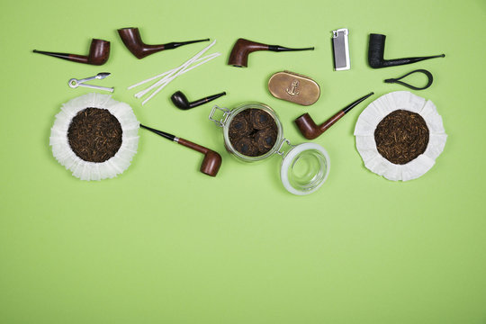 Different smoking tobacco pipes and pipe smoking accessories on green background. Top view.