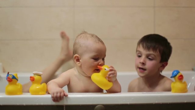 Little baby boy, playing with rubber ducks in bathtube with his siblings