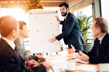 Meeting with chinese businessmen in office. Man is showing board with graphs and charts.