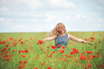 Naklejka na ściany i meble a natural woman with blond hair whirls in a field with beautiful red poppies. An atmosphere of carefree joy of happiness. 