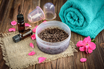 Coffee body scrub, sugar and coconut oil, essential oils, massage vacuum jars on dark wooden rustic table with pink flowers. Homemade cosmetic for peeling and spa care.