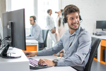 Smiling handsome customer support operator agent with hands-free device working in call center