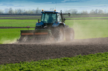 Fototapeta premium Blue tractor equipped with harrow working on the field at sundown.