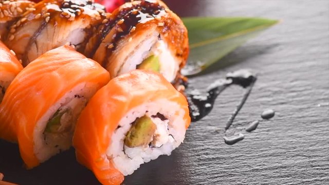 Sushi roll set on black slate background. Rotated rolls with salmon, tuna, eel, flying fish caviar closeup. Japan restaurant menu. 4K UHD video footage. 3840X2160