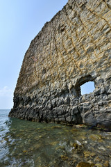A beautiful and unusual rock in the sea, vertical, flat, high on a blue sky background. Her name 