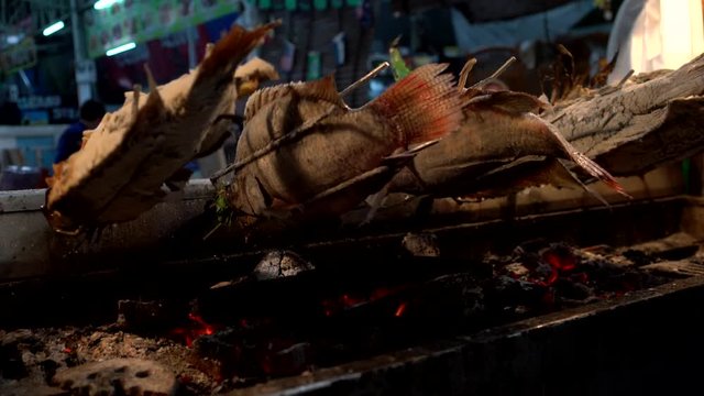 Fische mit Salzkruste drehen sich auf einem Holzkohlengrill in einer typischen Gark&uuml;che in einem Nachtmarkt in Thailand, Asien