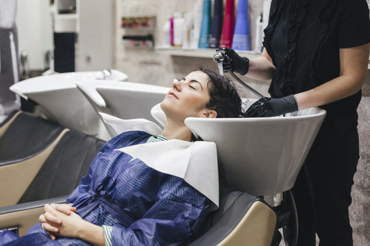 Beautiful young woman to hairdresser while washing head in hair salon