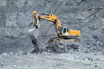 Crawler excavator Liebherr while working out on the quarry, against the backdrop of a rocky slope