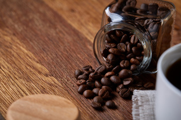 Roasted coffee beans get out of overturned glass jar on homespun tablecloth, selective focus, side view