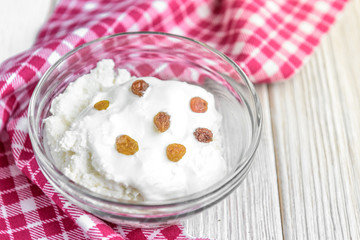 Cottage cheese with sour cream and raisins on white wooden background. 
