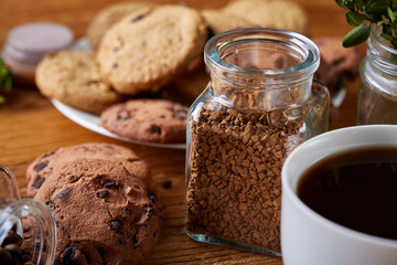 Coffee cup, jar with coffee beans, cookies over rustic background, selective focus, close-up, top view