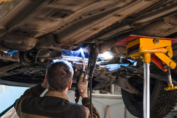 serviceman welds silencer on car by argon welding