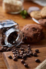 Roasted coffee beans get out of overturned glass jar on homespun tablecloth, selective focus, side view